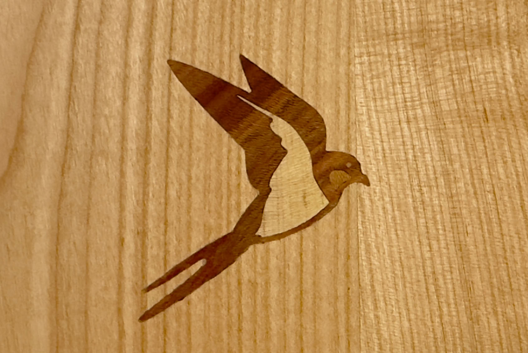 incrustation d'une hirondelle stylisée sur une surface en bois.