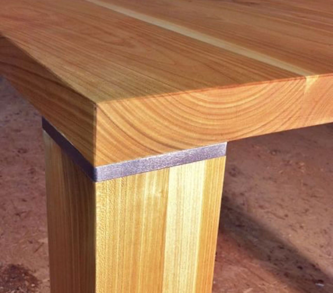 Table en bois avec un plateau épais et un pied carréavec insertion d'une partie métallique entre le pied et le plateau.