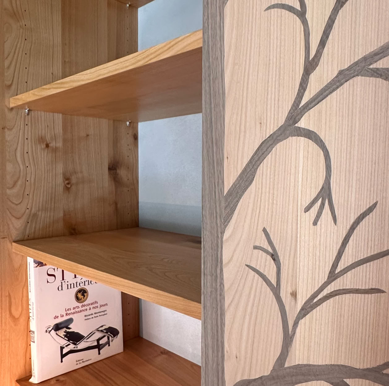 Bibliothèque en bois avec des étagères  et un motif de branches d'arbre en marquetterie.
