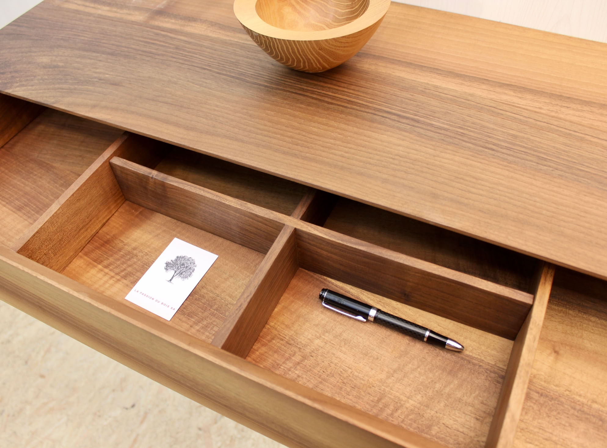 Console, tiroir en bois ouvert avec des compartiments contenant une carte et un stylo, bol en bois sur le dessus.